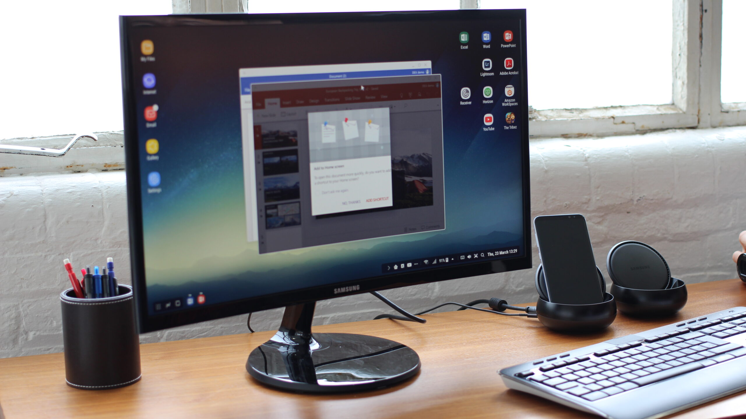 Samsung Galaxy S8 plugged into DeX docking station showing Android desktop mode on monitor